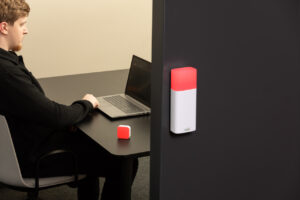 Luxafor busy light indicator for office door mounted on a meeting room wall, glowing red to show the room is occupied